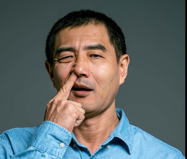 Man wearing blue denim shirt picking nose