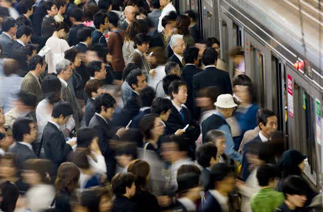 A crowd dressed for work, many looking at smart phones, packs a subway platform in Japan.