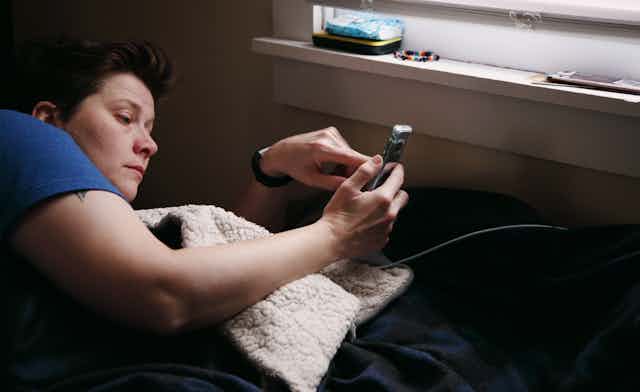 Person lays on their bed, a finger to their phone