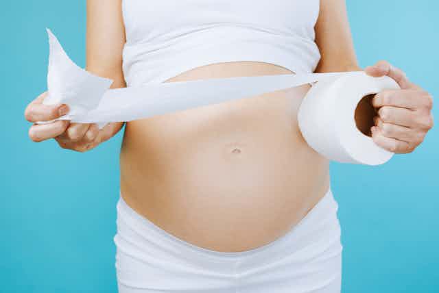 Pregnant woman pulling toilet paper off toilet roll