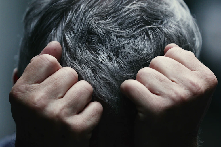 puños cerrados presionando una cabeza con pelo gris.