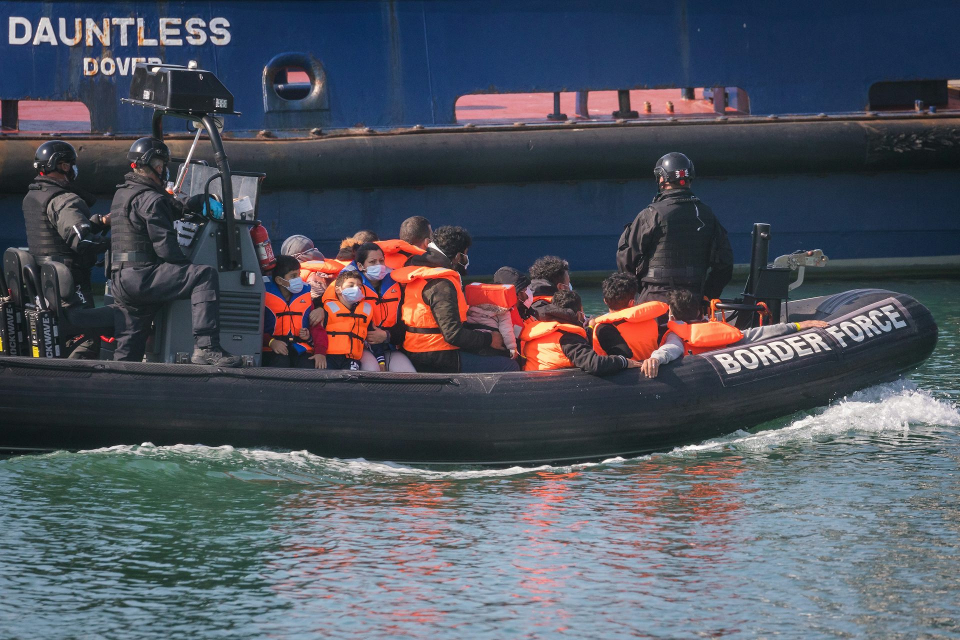 A small Border Force boat carrying a group of people in orange life jackets