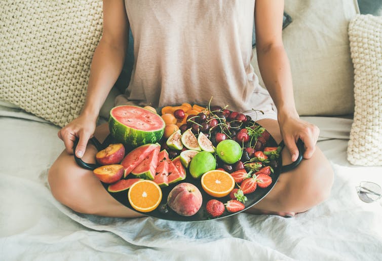 A woman holds a large platter of fruits.