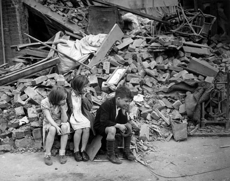 Children sit among the rubble of houses destroyed in the Blitz, London 1941.