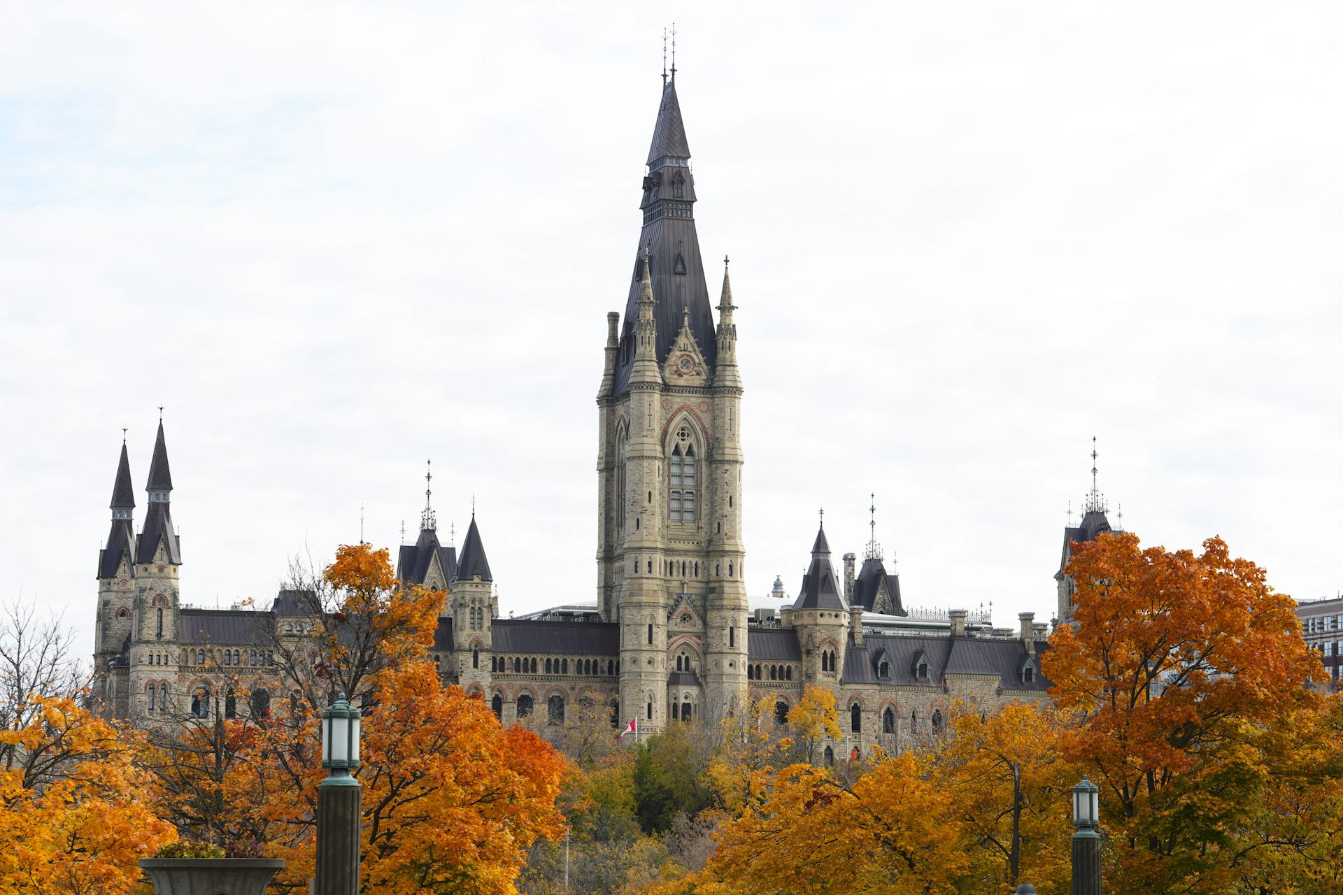 The West Block of Parliament Hill is pictured with orange, yellow and red trees framing it.