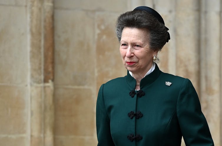 Princess Anne in a green coat and hat in front of a stone wall