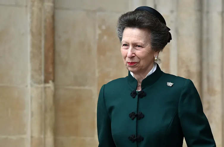 Princess Anne in a green coat and hat in front of a stone wall
