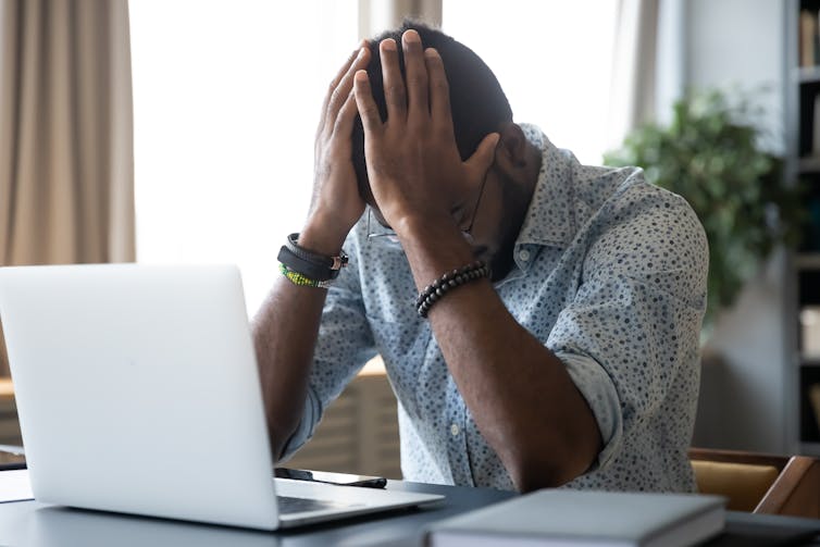 A young man sitting in front of a laptop with his head in his hands