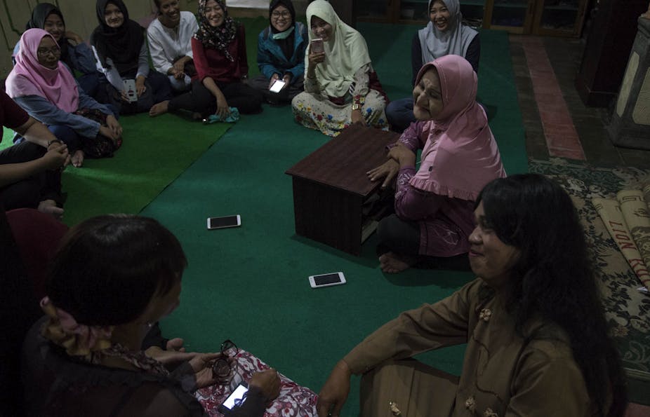 Women wearing colorful headscarves seated in a circle on a green carpet.