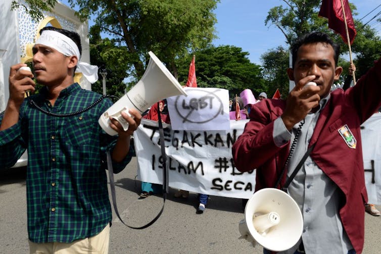 Protestors holding loudspeakers marching while holding a banner.