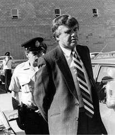 A black-and-white photo shows a man in a suit in handcuffs.