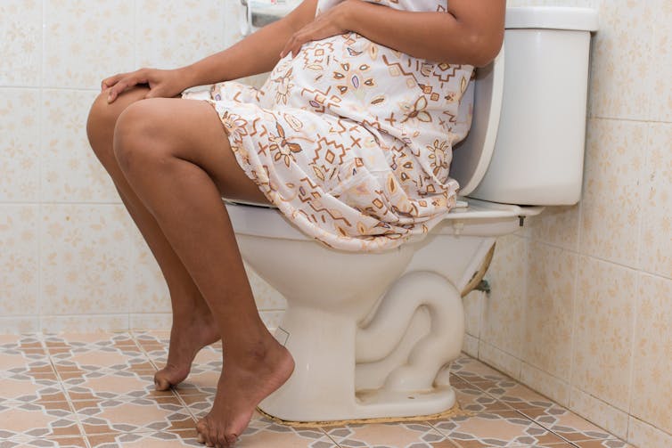Pregnant women sitting on toilet, holding tummy