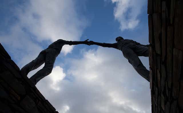 Statue of two men reaching across a divide. 