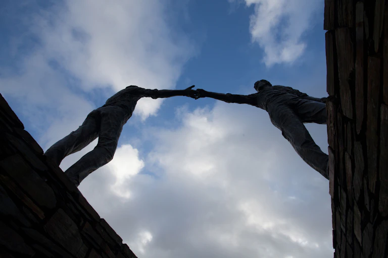 Statue of two men reaching across a divide.