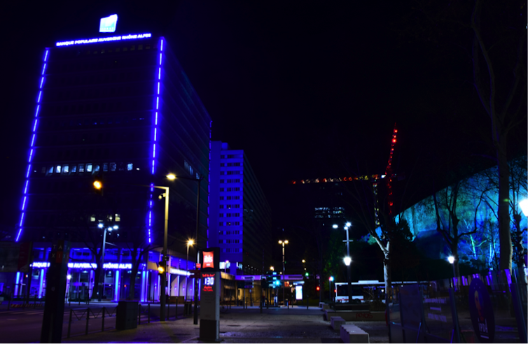 Dans le quartier d’affaires de la Part-Dieu, à gauche la tour d’une banque violemment éclairée de barreaux de diodes bleues, couleur de la banque ; et à droite une façade de l’auditorium de Lyon, mis en valeur par un projet d’éclairagiste, en bleu également