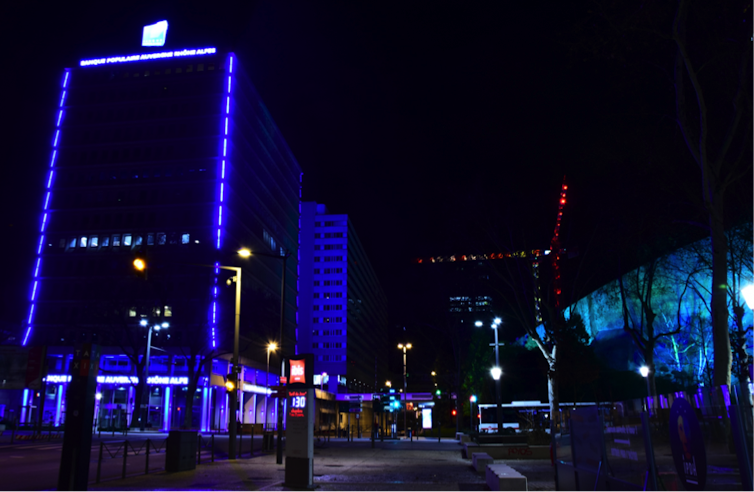 Dans le quartier d’affaires de la Part-Dieu, à gauche la tour d’une banque violemment éclairée de barreaux de diodes bleues, couleur de la banque ; et à droite une façade de l’auditorium de Lyon, mis en valeur par un projet d’éclairagiste, en bleu également