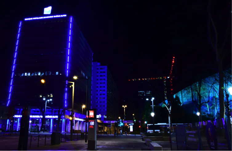 Dans le quartier d’affaires de la Part-Dieu, à gauche la tour d’une banque violemment éclairée de barreaux de diodes bleues, couleur de la banque ; et à droite une façade de l’auditorium de Lyon, mis en valeur par un projet d’éclairagiste, en bleu également