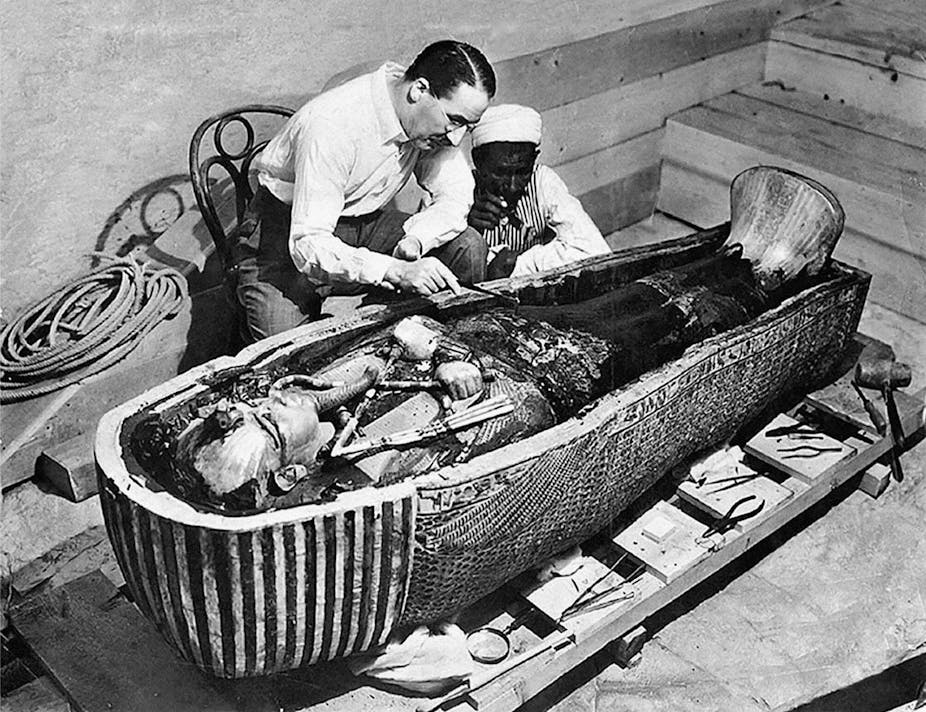 Two men looking into a sarcophagus. 