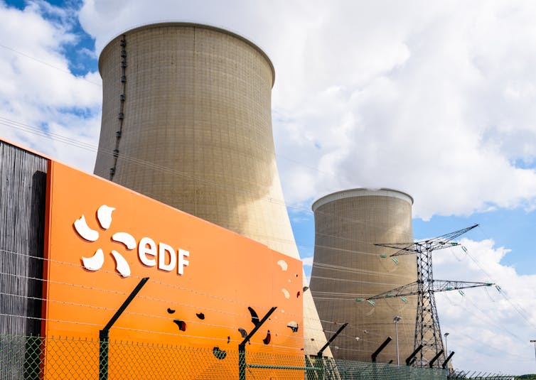 A close-up of an orange EDF sign against the backdrop of two large cooling towers.
