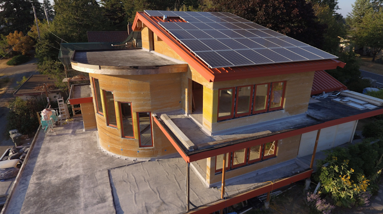 A large modern design house made of wood and hempcrete with trees in the background.