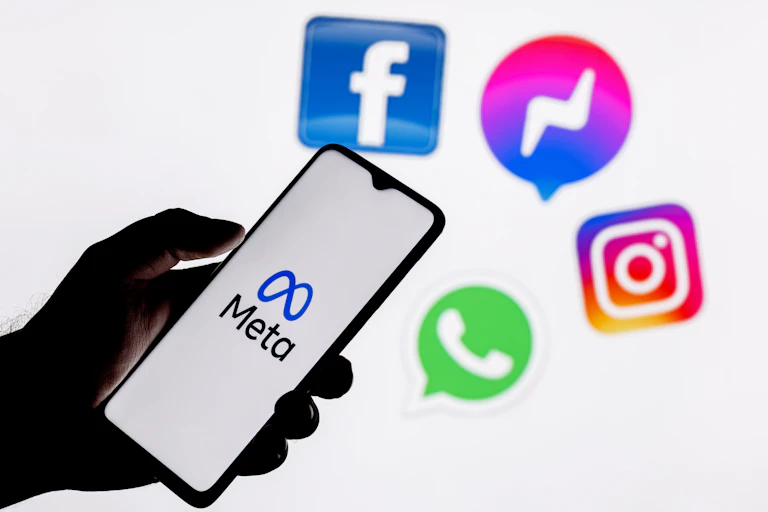 Hand holding phone with meta logo on screen, Facebook, Messenger, Instagram and Whatsapp logos in background