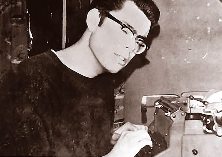 A young man in glasses by a typewriter.