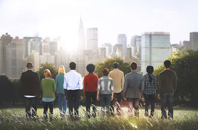 A row of people standing with their backs to the camera facing a city in the distance
