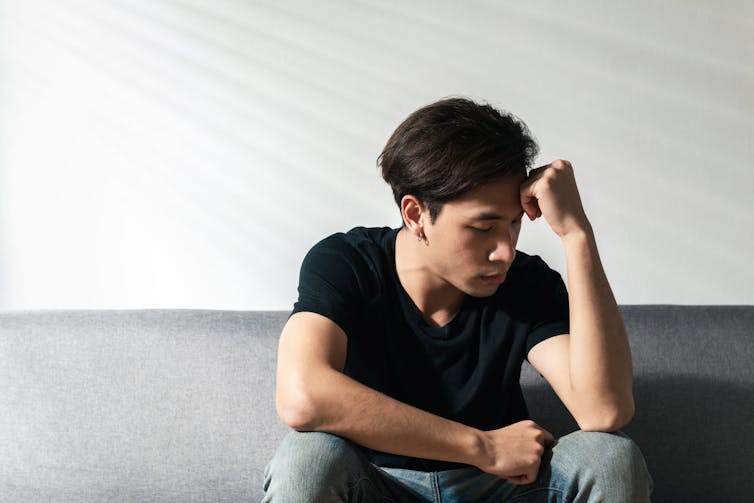 A young man sitting on a sofa, appears despondent.