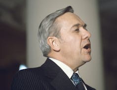 A grey-haired man is seen in profile as he makes a speech.