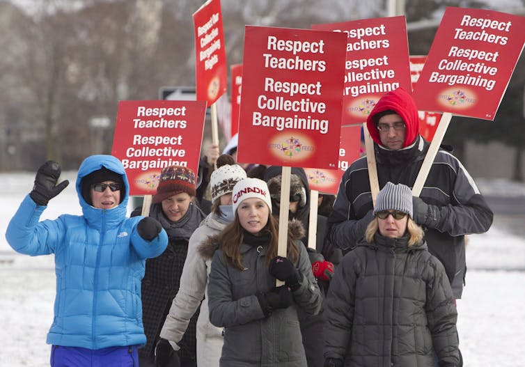 Men and women in parkas and hats carry red signs that read Respect Collective Bargaining.