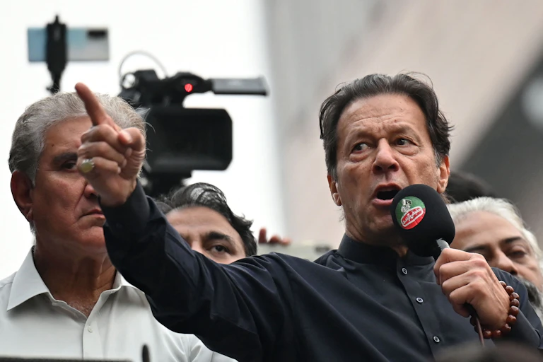A man in a black shirt points with his finger while speaking into a microphone.