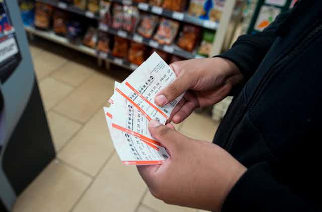close up of white hands holding several lottery tickets in a convenience store