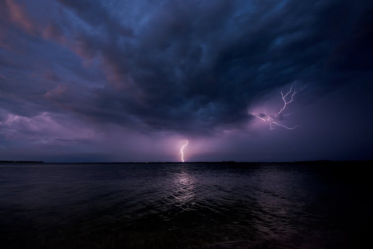 a bolt of lightning can be seen on the horizon in the clouds above the sea