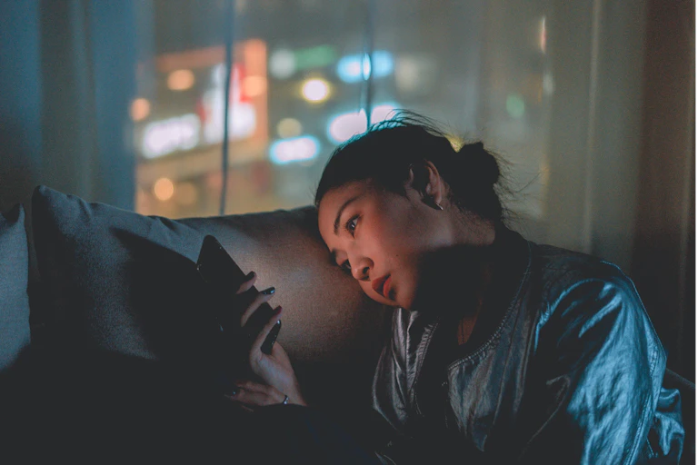 Teenager scrolling phone at night on sofa