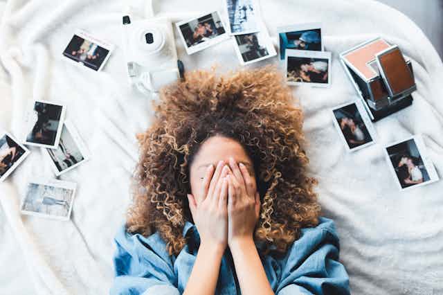 Woman lying on the bed covering her face, surrounded by photos