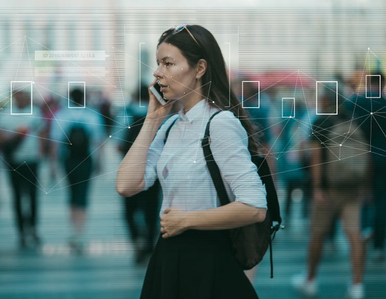 Woman on phone while numerous people behind her are being scanned by facial recognition technology