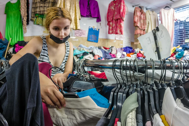 Una mujer rubia con mascarilla rebusca entre burros de ropa usada.