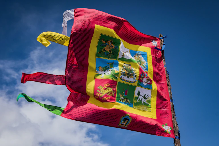 A red and yellow Buddhist prayer flag flapping against a bright blue sky.