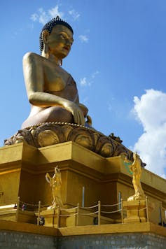 A huge golden Buddha statue against a bright blue sky.