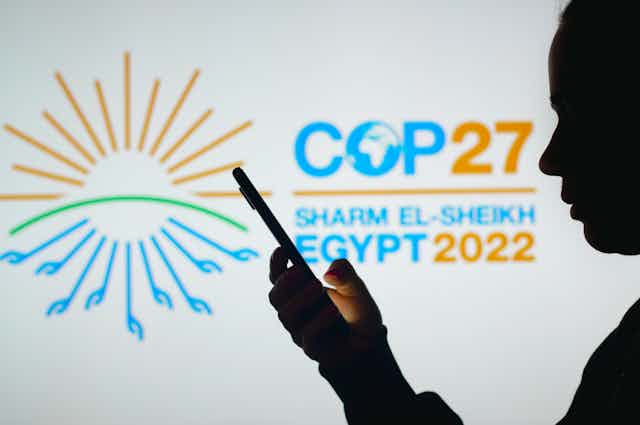 Silhouette of man on phone in front of COP27 sign