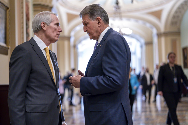 Two men in dark suits talk in a high-ceilinged, elegant public space.