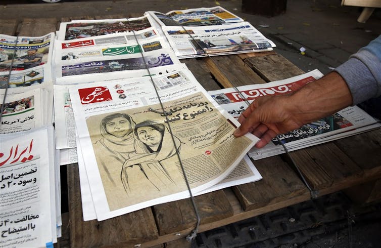 An Iranian man picks up a copy of Iranian daily newspaper Hammihan with a drawing featuring two Iranian female journalists Niloufar Hamedi and Elaheh Mohammadi, who have been arrested for covering the protests.