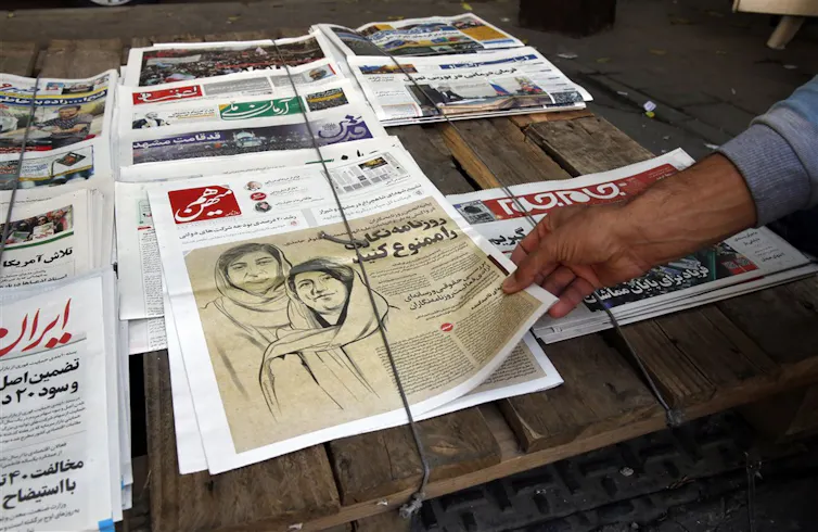 An Iranian man picks up a copy of Iranian daily newspaper Hammihan with a drawing featuring two Iranian female journalists Niloufar Hamedi and Elaheh Mohammadi, who have been arrested for covering the protests.