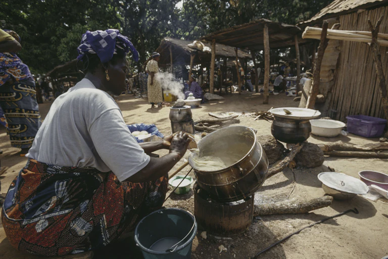 Woman seated in front of large pot cooking on fire.