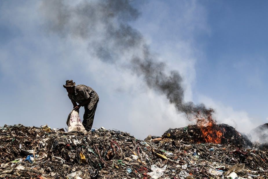 Man picking trash from dumpsite near burning refuse.
