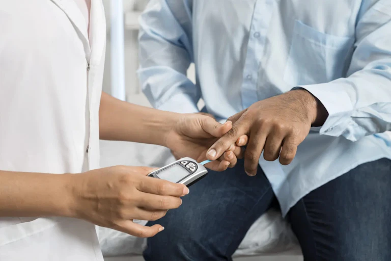 Cropped image of hands of a health-care worker in white coat using a glucometer on the finger of a person in a blue shirt.