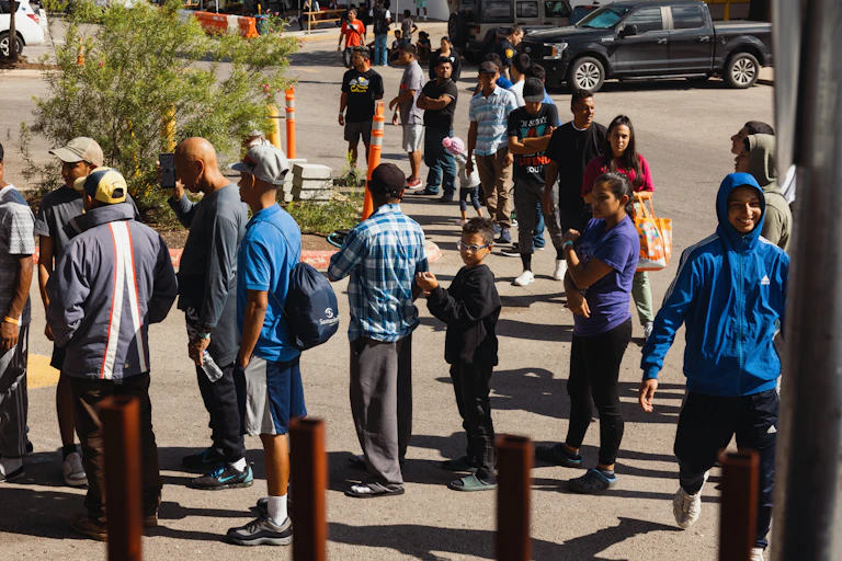 A group of men, women and children wait outside in line to receive food from a charity.