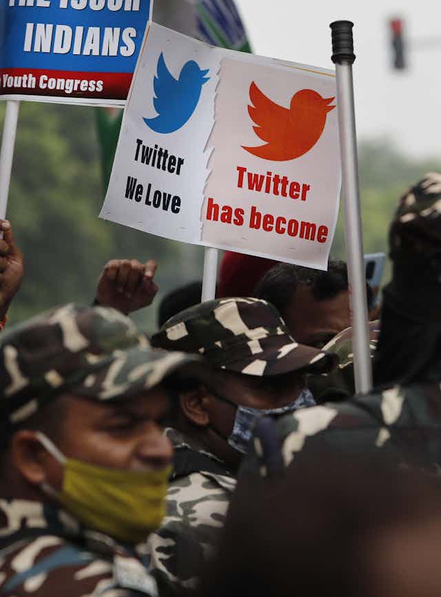 A photo of protesters in camouflage gear holding signs criticising Twitter.