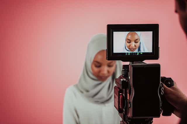 A woman in a hijab is framed by a camera lens.