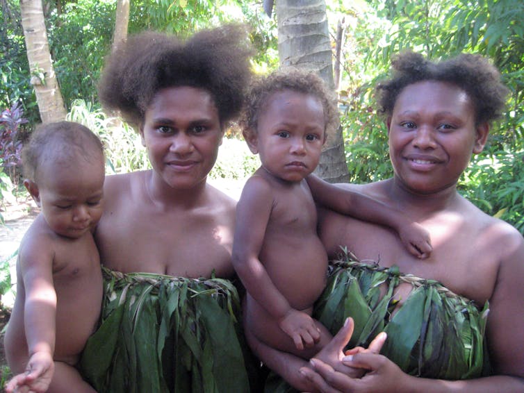 two women in traditional dress hold babies